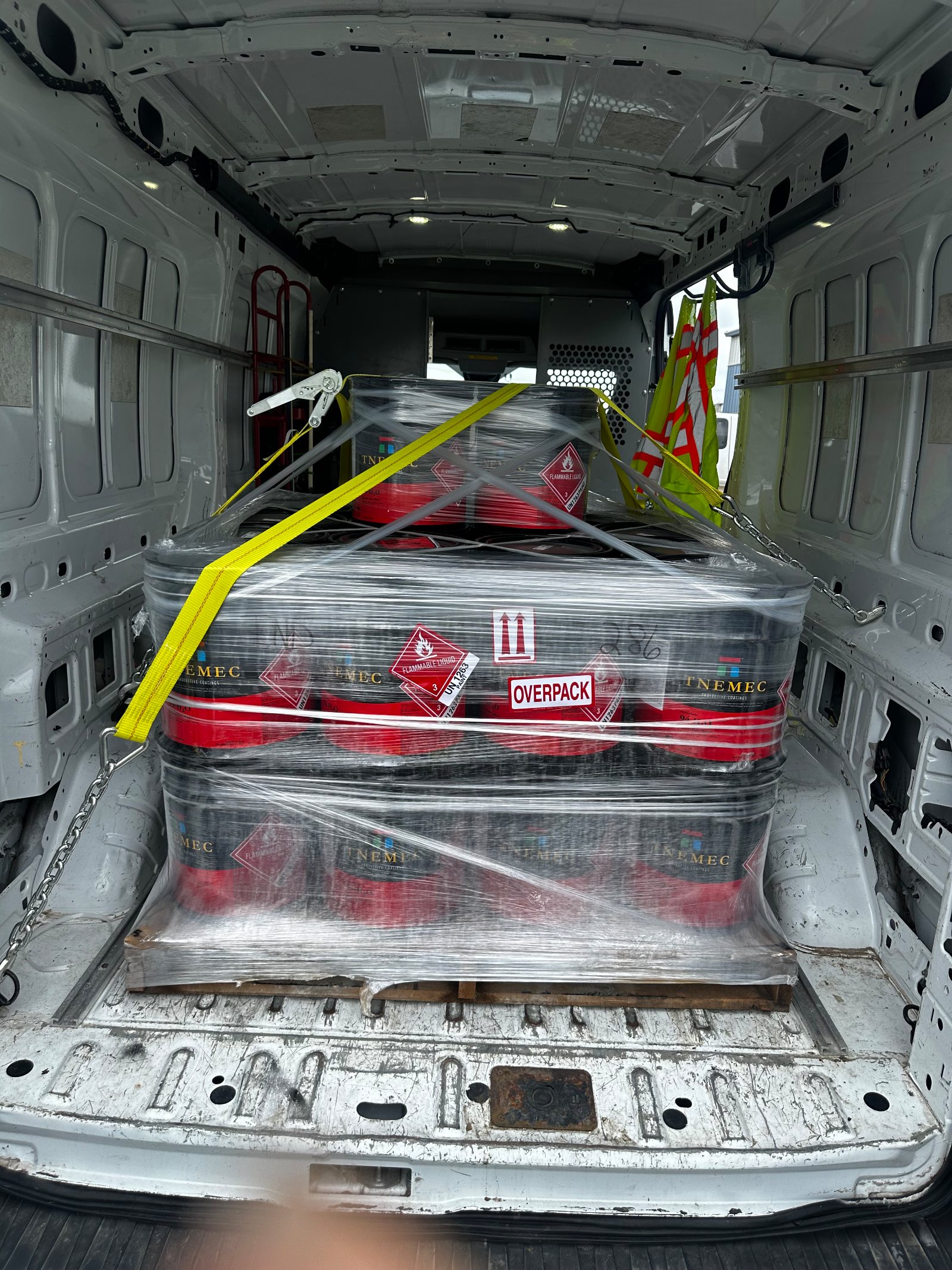 The client's own daylight frame through the open rear doors: a shrink-wrapped pallet of coating pails, hazmat-placarded