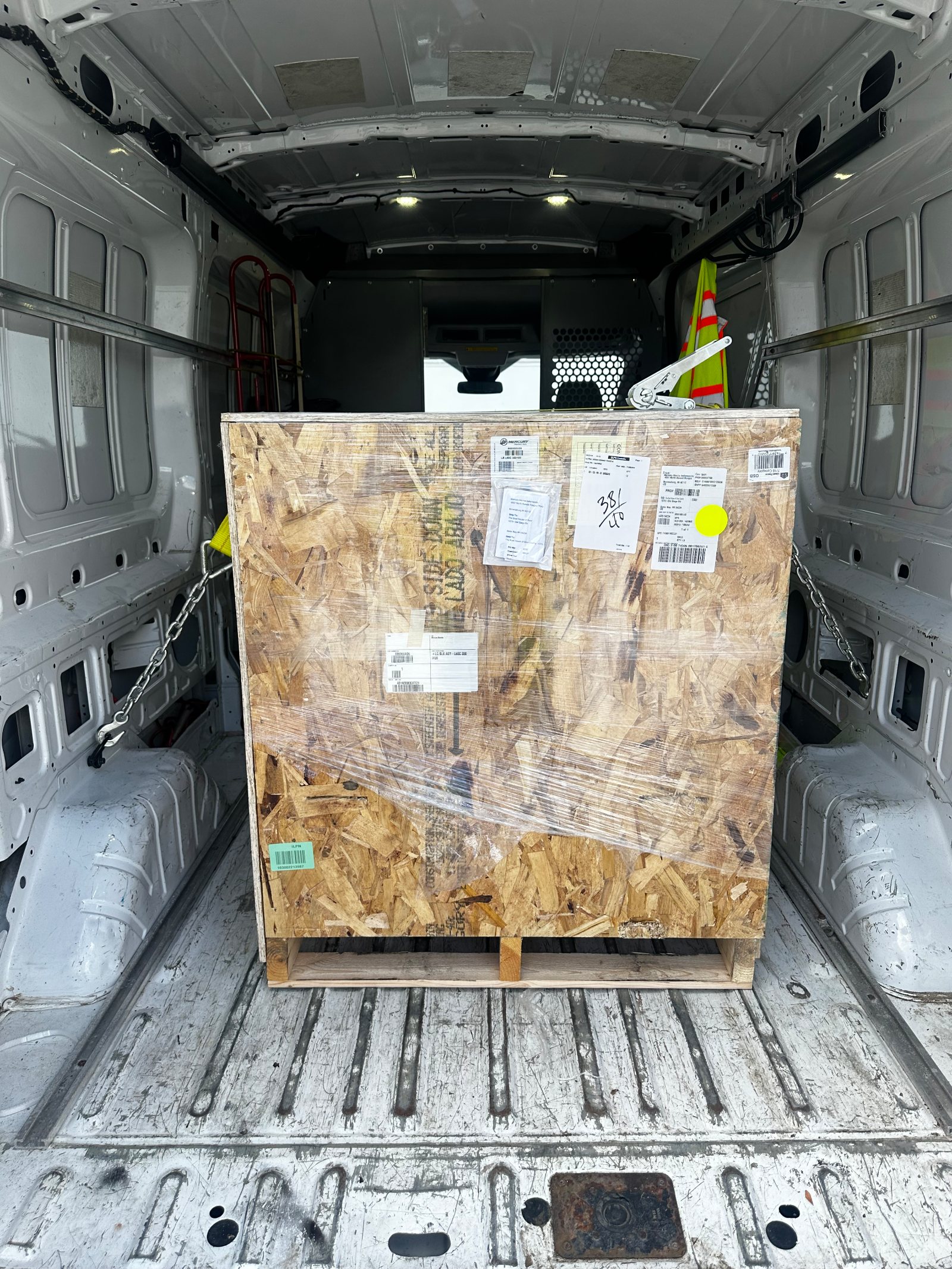The client's own daylight frame of the same van's bay: a large shrink-wrapped OSB crate on a pallet, chained to the wall